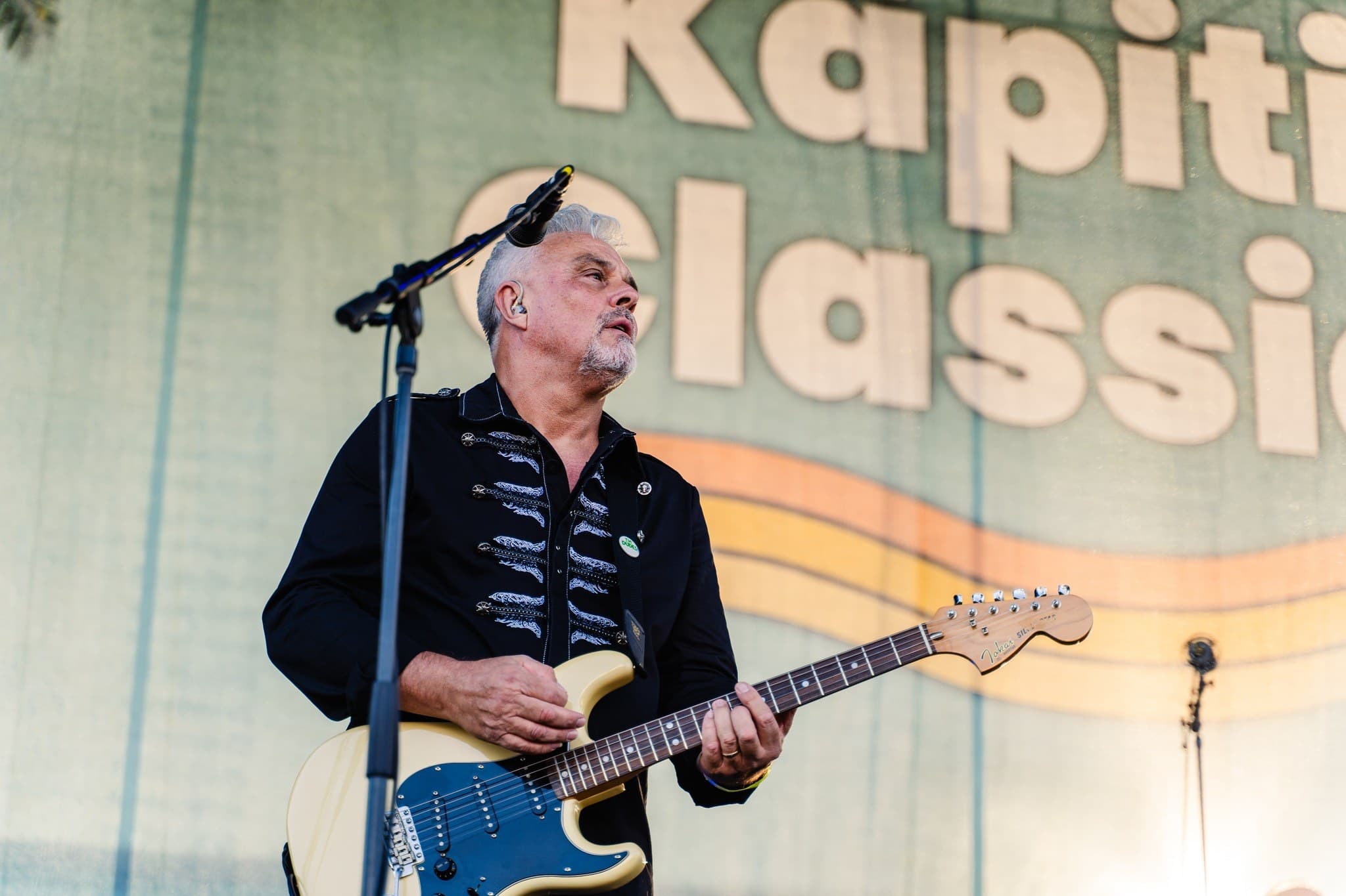Rikki on stage with a blue Stratocaster at the Kapiti Classic